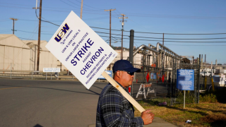 An operator walks with a picket sign outside an entrance to the Chevron Corp. refinery